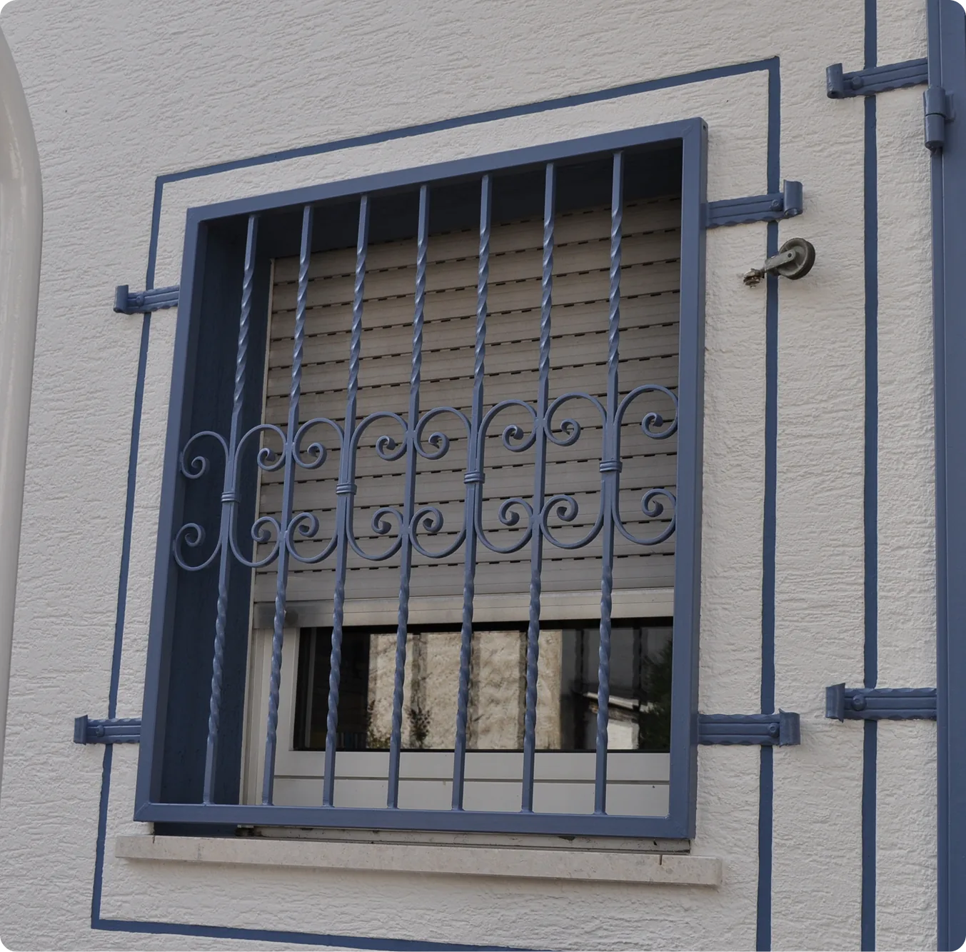 Lackiertes blaues Fenstergitter mit Zierelementen an einer Putzfassade