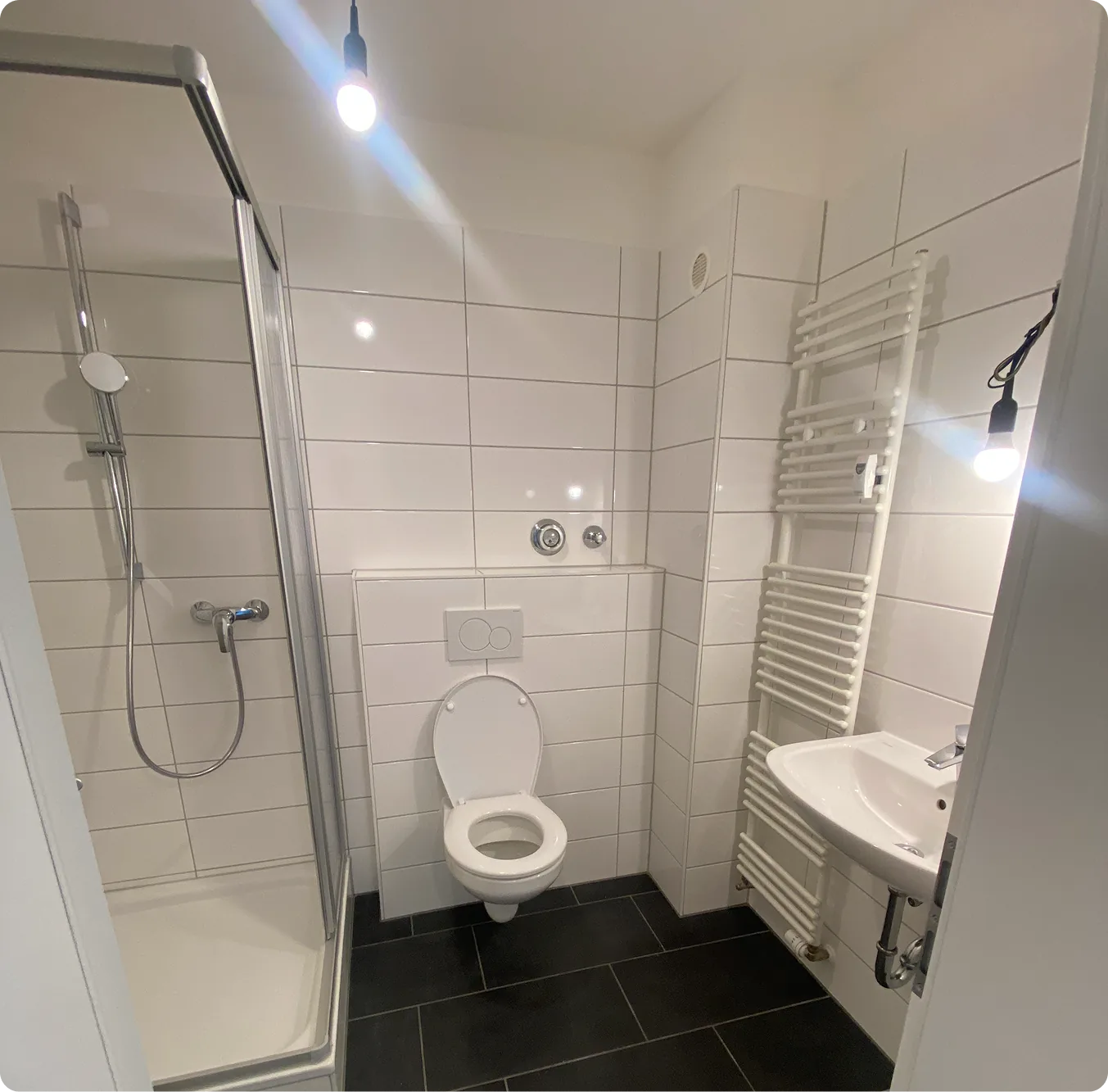 Nachher: Fertiges Bad mit weißen Fliesen, Dusche, WC und Handtuchheizkörper