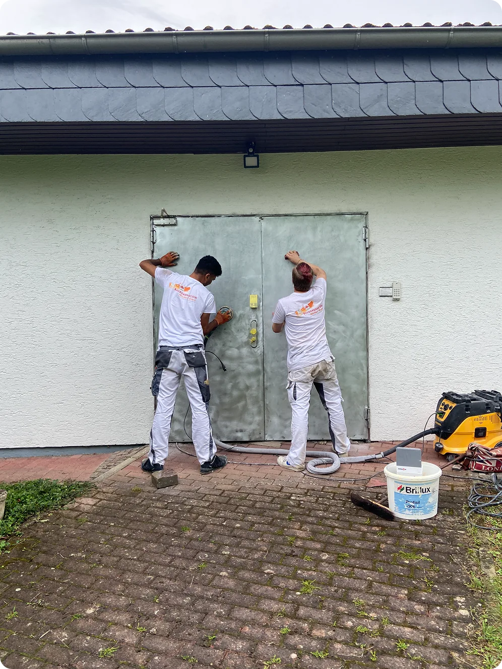 Zwei Maler schleifen eine Stahltür vor dem Lackieren