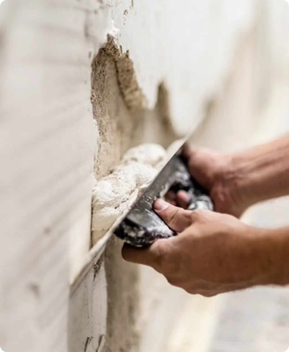Handwerker trägt Putz mit der Kelle auf eine beschädigte Wand auf