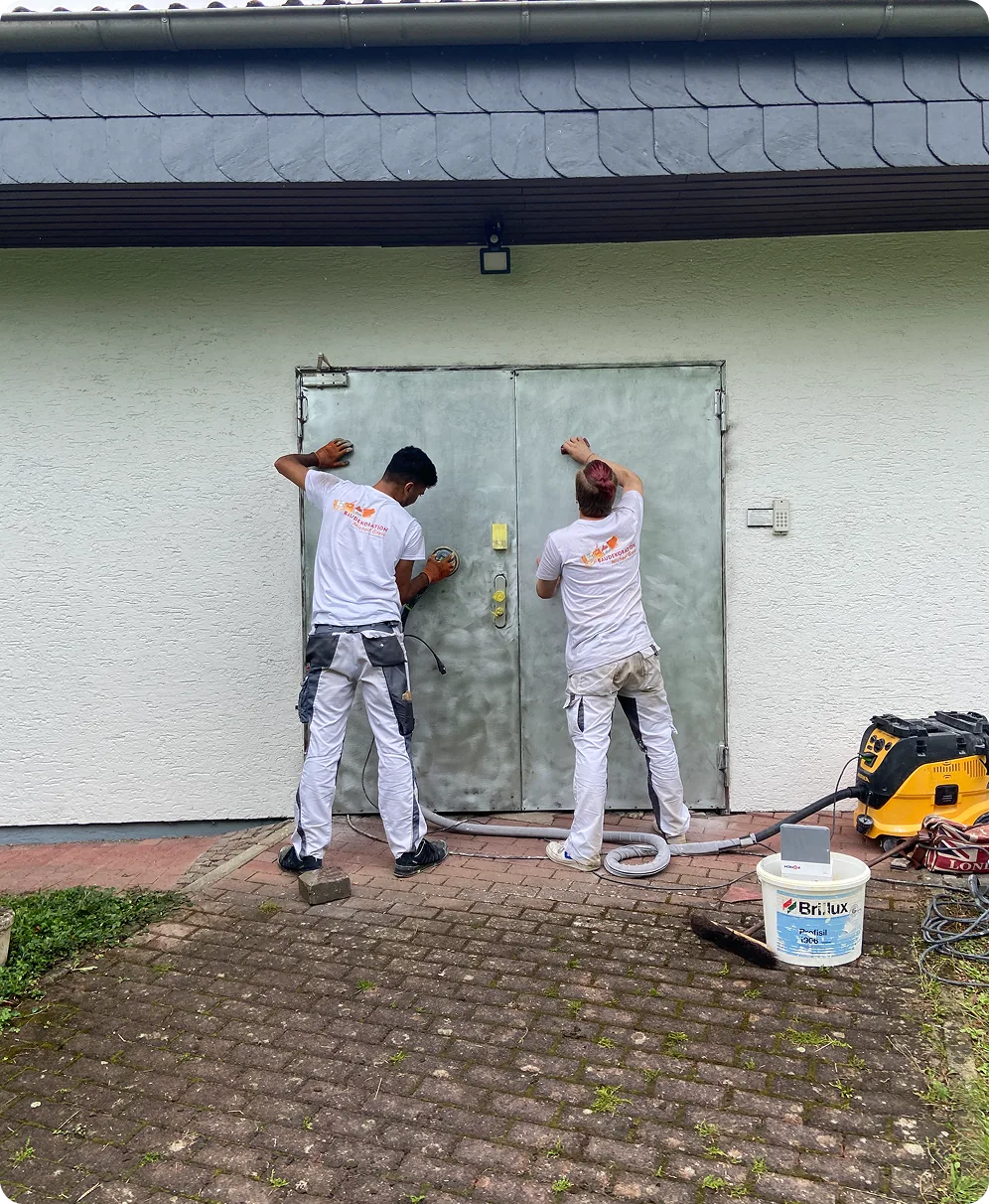 Zwei Maler schleifen eine Stahltür an, daneben Absauggerät und Farbeimer