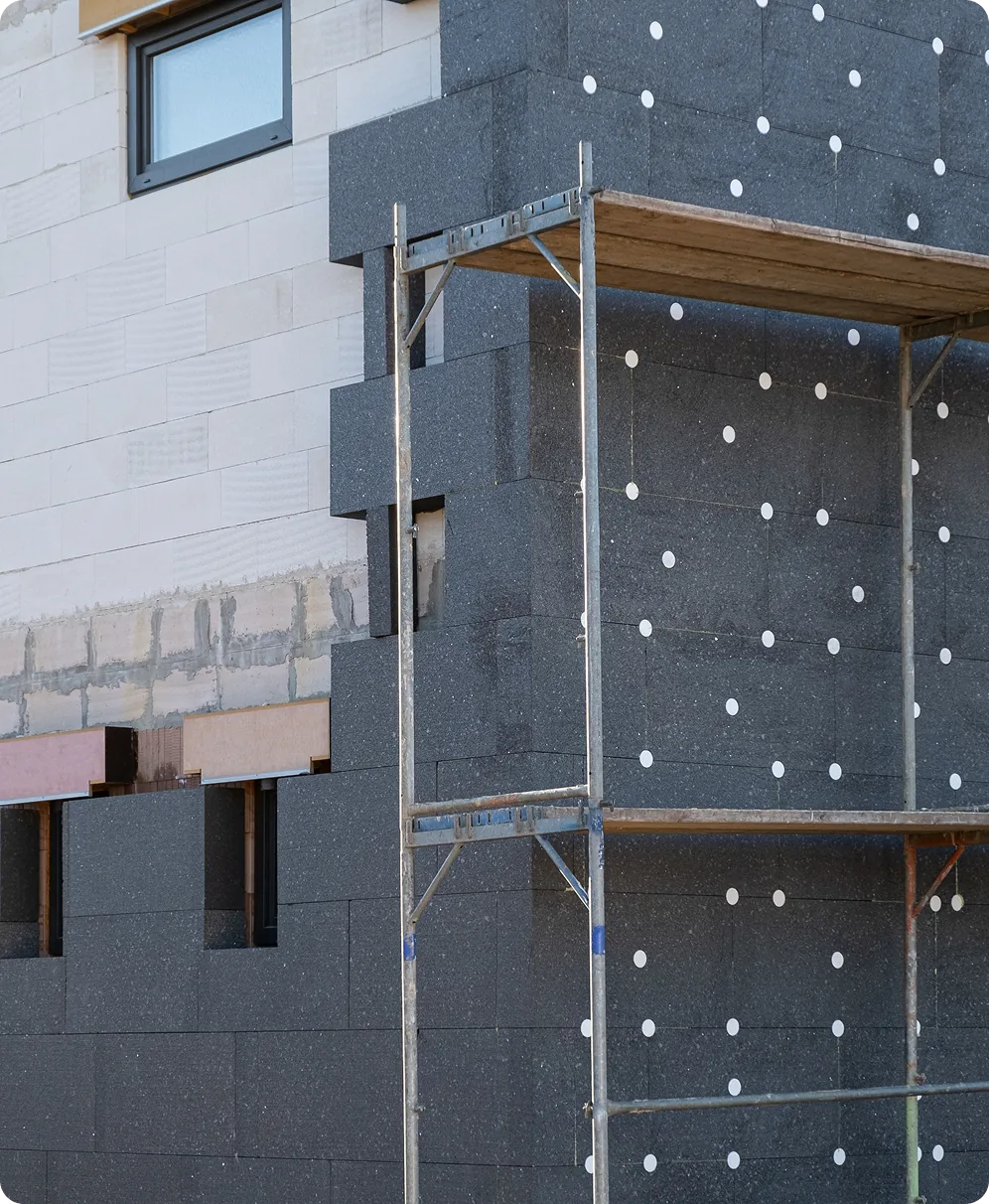Fassade mit grauen Dämmplatten und Dübeln, davor ein Gerüst