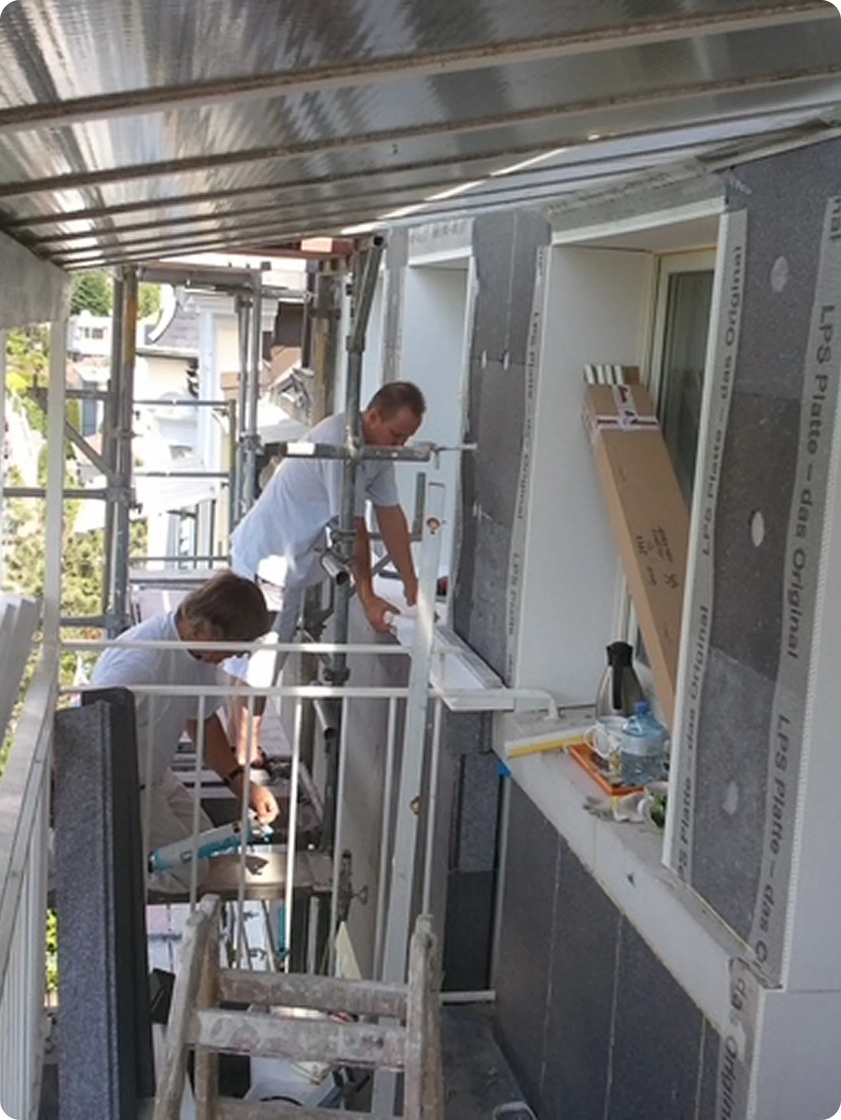Zwei Handwerker montieren Dämmplatten auf dem Gerüst an einer Fassade