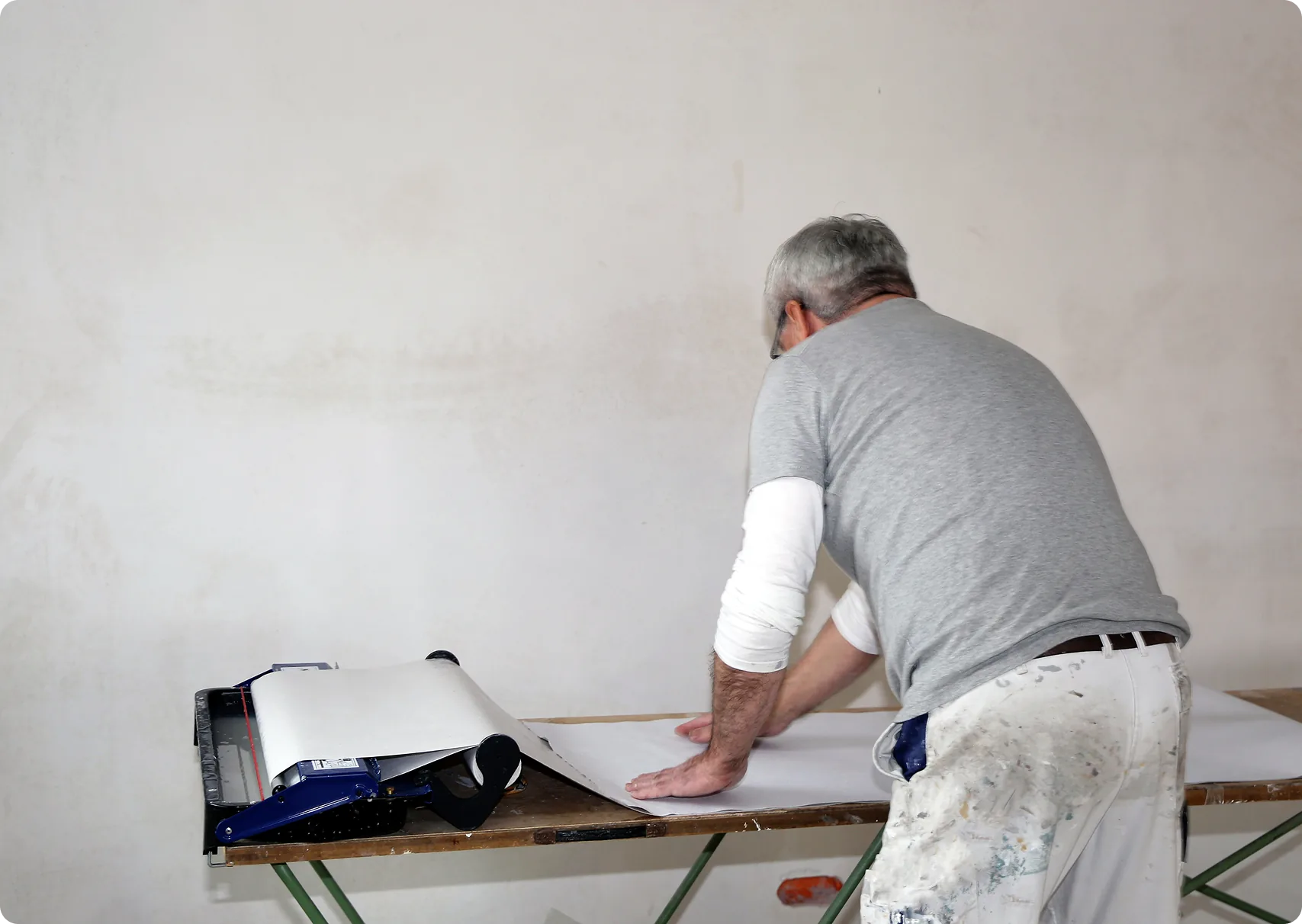 Maler kleistert Tapete mit dem Tapeziergerät auf dem Tisch ein